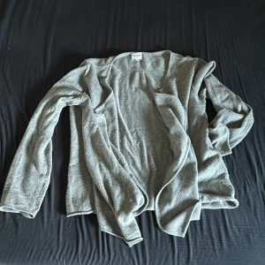 Grå kashmirtröja från TAUP - Säljer en supermjuk och lyxig grå tröja från TAUP, tillverkad i 100% kashmir. Perfekt för kyliga dagar med sin omlott-design som ger en elegant touch. Tröjan har långa ärmar och är i ett neutralt grått som passar till allt. Made in Nepal, så du vet att kvaliteten är på topp!