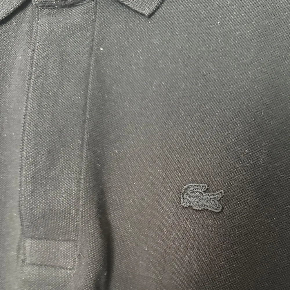 Säljer en klassisk svart pikétröja från Lacoste. Den har en stilren design med korta ärmar och den ikoniska krokodilloggan på bröstet. Perfekt för både vardag och lite mer uppklädda tillfällen. Tröjan är i bra skick och redo för en ny ägare!vikitg in. Tröjor & Koftor.