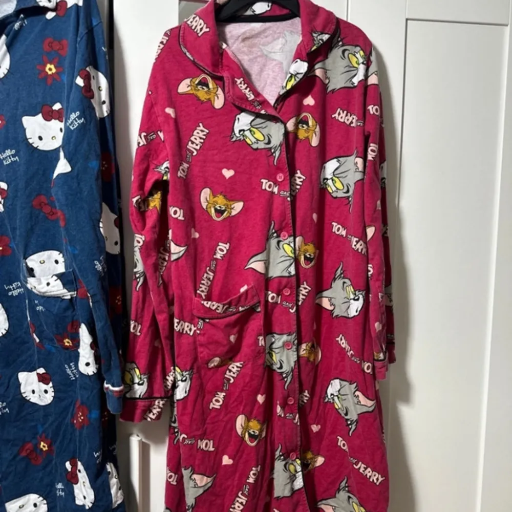 Säljer två mysiga pyjamasar med roliga motiv! Den blåa har ett Hello Kitty-mönster med röda blommor och rosetter, medan den rosa har ett Tom & Jerry-mönster med hjärtan. Båda är långärmade och perfekta för en chill kväll hemma. De har knappar framtill och praktiska fickor.. Klänningar.