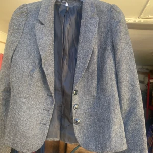 Grå kavaj med knappar - Säljer en stilren grå kavaj med tre knappar framtill. Den har en klassisk passform och är perfekt för både vardag och fest. Materialet känns robust och har en fin textur. Kavajen är fodrad vilket ger extra komfort.