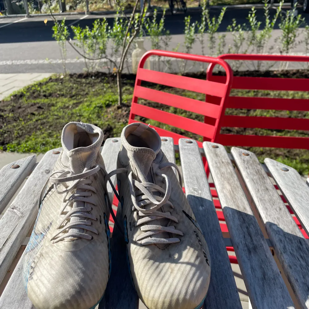 Säljer ett par Nike Mercurial fotbollsskor i en stilren beige färg med blå och röda detaljer. Skorna har snörning och är designade för att ge bra grepp på planen. De är i välanvänt skick men fortfarande funktionella för träning eller match.. Skor.