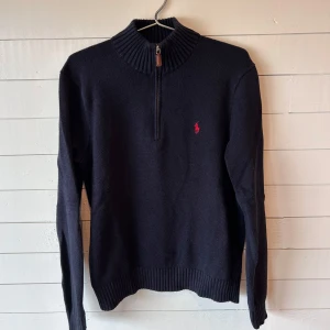 POLO Ralph Lauren Mörkblå Half Zip Pullover, Storlek L - Mörkblå half zip pullover i storlek L från Polo Ralph Lauren i bra skick. Inga defekter eller fläckar förutom att lappen inne i tröjan har släppt i ena änden (se bild 4). Tröjan är nytvättad och kommer från ett djur- och rökfritt hem. Nypris: 1390kr 