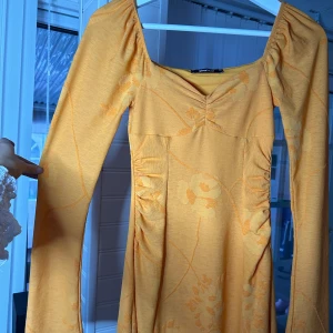 Orange klänning från Gina Tricot - Säljer en superfin orange/gul klänning från Gina Tricot. Den har ett subtilt blommönster och långa ärmar. Klänningen har en v-ringad & materialet känns mjukt och bekvämt🧡