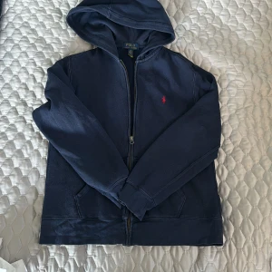 Ralph Lauren (zip hoodie) - Mörkblå Ralph Lauren zip hoodie i stl 14-16. Liten i storleken min son har haft den när han va ca 10 år uppskattar den till svensk stl 150 cm. Använd men bra skick. 