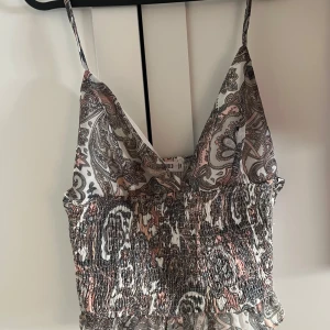Mönstrad topp från Missguided - Säljer en superfin mönstrad topp från Missguided. Den har ett paisleymönster i svart, vitt och lite rosa. Toppen är ärmlös med smala axelband och har en smockad, croppad passform som ger en snygg siluett. Perfekt för sommardagar eller en festkväll! 🌸