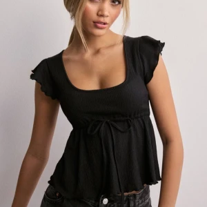 Svart topp med volangärmar - Som ny aldrig använd! Säljer en superfin svart topp med volangärmar. Den har en söt knytning framtill och är perfekt för både vardag och fest. 
