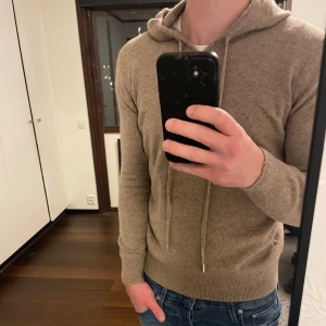 Beige Merinoull hoodie - En riktigt bekväm och stilren beige hoodie i 100% merinoull. Storlek S, men passar S-XS. Hoodien är sprillans ny och har inga defekter. Snörerna går att förkorta vid önskan. Tveka inte att höra av dig vid funderingar!