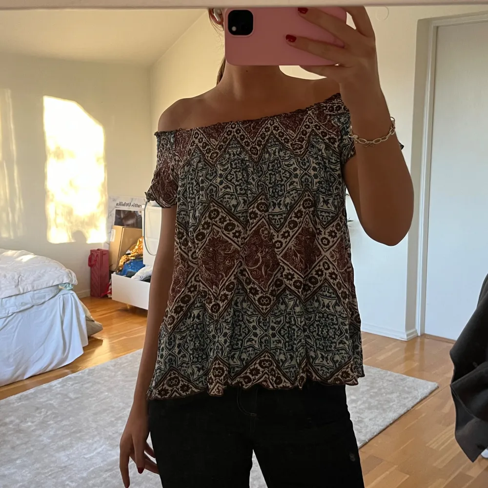 Snygg offshoulder topp med ett unikt mönster i jordnära färger. Perfekt för en avslappnad stil med en bohemisk touch. Toppen har en lös passform och korta ärmar.. Yläosat.