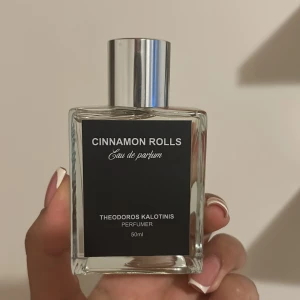 Cinnamon Rolls Eau de Parfum - Upptäck doften av nybakade kanelbullar med denna Eau de Parfum från Theodoros Kalotinis. Flaskan rymmer 50 ml och har en stilren design med en svart etikett och silverfärgad kork. Perfekt för dig som älskar söta och kryddiga dofter.