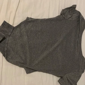 Grå glittrig bodysuilt - Snygg grå bodysuilt med glittrigt material och korta ärmar. Perfekt för en kväll ute eller en speciell tillställning. Toppen har en figurnära passform som framhäver silhuetten.