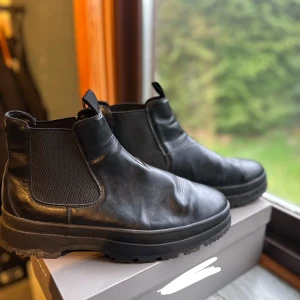Svarta Chelsea Boots - st45 - Snygga svarta Chelsea boots i skinn med elastiska paneler på sidorna för enkel på- och avtagning. Perfekta för både höst och vinter med en robust sula som ger bra grepp.