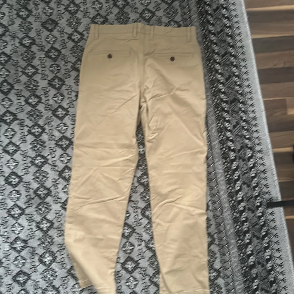 Snygga beige chinos från H&M med normal passform. Byxorna har knappar och bälteshällor, vilket gör dem perfekta för en stilren look. De är tillverkade i ett bekvämt bomullsmaterial.. Farkut & Housut.