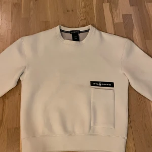Vit tröja från Sail Racing - Säljer en stilren vit tröja från Sail Racing i storlek S-M Tröjan har en enkel design med en bröstficka och Sail Racing-logga. Perfekt för en avslappnad stil. Ny pris 1300 kr!