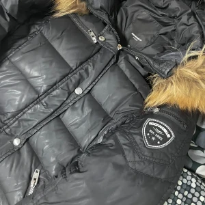 Rockandblue jacka  - Snygg svart dunjacka från Rockandblue med pälsdetaljer på huvan. Jackan har dragkedja och knappar framtill samt flera praktiska fickor. Perfekt för kalla vinterdagar. Värmer cok bra 