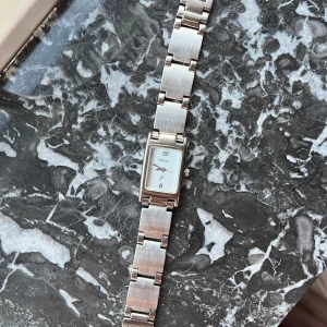 Silverfärgad klocka från Fossil - Elegant silverfärgad klocka från Fossil med rektangulär urtavla och stilren design. Armbandet är i metall och har en klassisk länkstil. Perfekt för en tidlös look.