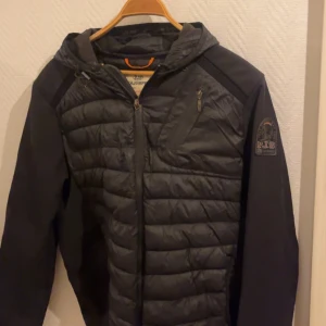 Parajumpers Cardigan - Snygg svart jacka från Parajumpers med quiltad design och dragkedja. Jackan har en huva och en bröstficka med dragkedja. Perfekt för kyligare dagar. ✅ Xl men Sitter definitivt som L