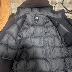 Svart dunjacka från The North Face - Säljer en svart dunjacka från The North Face med dragkedja och praktiska fickor. Jackan har en normal passform och är perfekt för kalla dagar. Den är långärmad och har en stilren design.