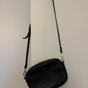 Crossbody väska, Wera, svart, skinn - Snygg svart crossbody väska från Wera, svart, 100% äkta läder. Väskan är i fint skick, små tecken på slitage, se bilder.  Justerbara band som även går att ta.   Mått:  Längd ca 18 cm Höjd ca 12 cm Djup ca 5,5 cm