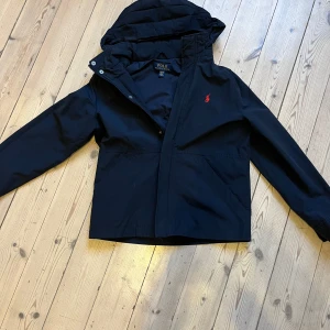 Svart jacka från Ralph Lauren - Snygg svart vindjacka från Ralph Lauren med huva och dragkedja. Jackan har bra skick, och passar Storlek 152. Skriv vid minsta lilla fundering! Pris kan diskuteras 