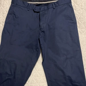 Mörkblå chinos från Riley - Snygga mörkblå chinos från Riley i slim fit. Tillverkade av 98% bomull och 2% elastan för en bekväm passform. Byxorna har knappar bak och bälteshällor för extra stil och funktionalitet. Storlek 52.