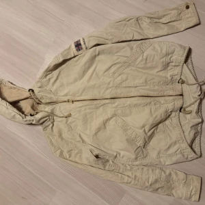 Beige jacka från Bondelid - Säljer en beige jacka från Bondelid med huva och dragkedja. Jackan har långa ärmar och praktiska fickor framtill. Perfekt för vår och höst.