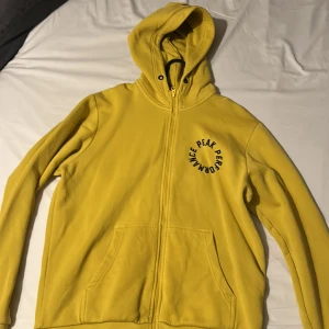 Gul hoodie från Peak Performance - Snygg gul hoodie från Peak Performance med dragkedja och tryck på bröstet. Perfekt för en avslappnad stil. Den har en praktisk huva och fickor framtill.