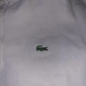 Säljer en klassisk vit pikétröja från Lacoste med den ikoniska krokodilloggan på bröstet. Tröjan har korta ärmar och en traditionell krage med knappar. Perfekt för en stilren och avslappnad look.pris kan förhandlas 