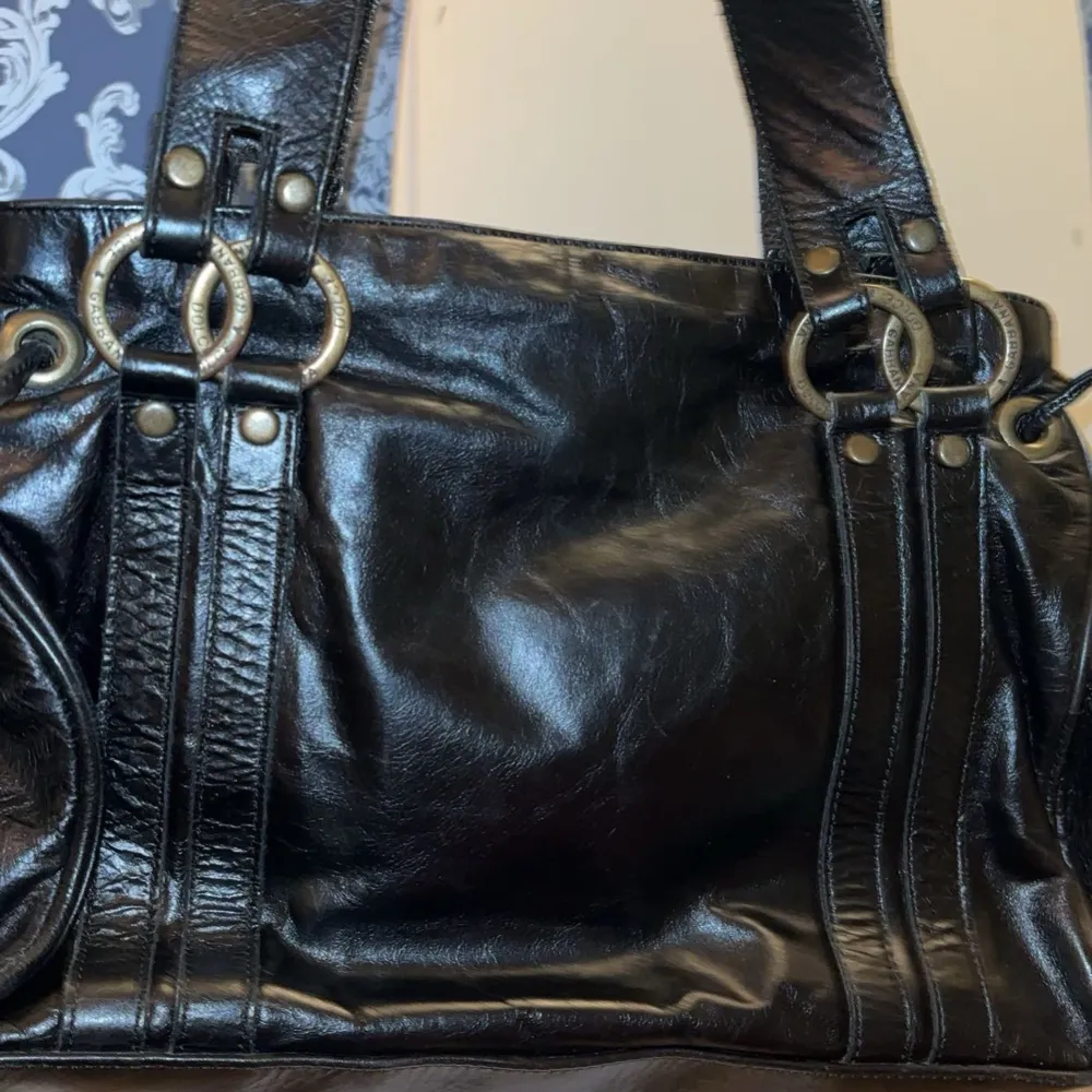 Snygg svart skinnväska från Dolce & Gabbana med dekorativa ringdetaljer och nitar. Väskan har dubbla handtag och en praktisk innerficka med dragkedja. Perfekt för att bära med sig det nödvändigaste med stil.. Laukut & Käsilaukut.