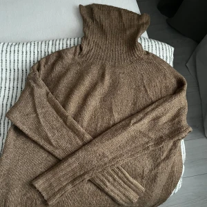 Brun stickad polotröja - Mysig brun stickad polotröja med långa ärmar. Perfekt för kyliga dagar med sin höga krage som håller dig varm. En klassisk och stilren design som passar till det mesta.