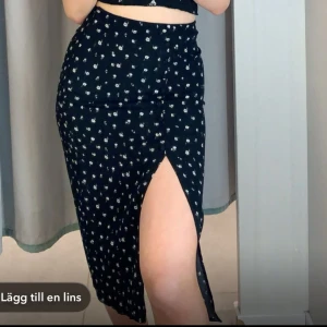 Svart blommig kjol med slits - Svart kjol med små vita blommor och en hög slits. Gullig till sommaren. Jag använde aldrig kjolen efter jag köpte den men kan skicka fler bilder om så önskas.
