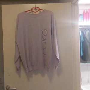 Ljuslila tröja från Quinto - Säljer en superfin ljuslila tröja från Quinto. Den har en avslappnad passform och är perfekt för både vardag och mysiga hemmakvällar. Tröjan har långa ärmar och ett coolt tryck på framsidan. Perfekt för dig som vill ha något bekvämt men ändå stilrent! 💜
