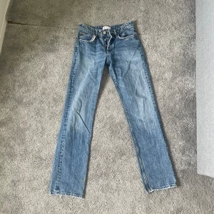 Blå jeans från Zara - Säljer ett par klassiska blå jeans från Zara i storlek XS. De har en straight passform och är perfekta för vardagsbruk. Jeansen är tillverkade i Bangladesh och har en snygg, enkel design med fem fickor och knappgylf.