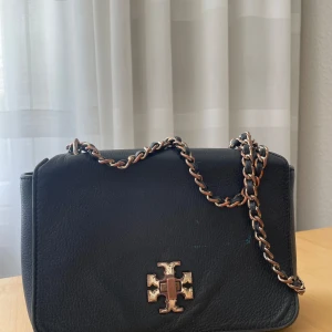 Tory Burch väska  - Använd vilket syns på metallen. All sömnad, inne i väskan som på utsidan är fortfarande i väldigt gott skick.  Lädret är i gott skick.  Tyvärr en blå,liten akrylfläck på framsidan - därav lågt pris på väskan.