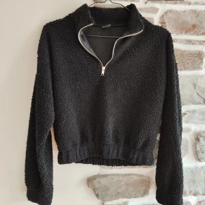 Svart fleece tröja från Gina Tricot - Mysig svart fleece tröja från Gina Tricot i storlek XS. Perfekt för kyliga dagar med sin mjuka och varma känsla. Tröjan har en dragkedja framtill och långa ärmar. Den är både stilren och bekväm, idealisk för höst och vinter.