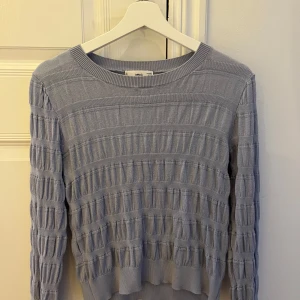 Ljusblå stickad tröja från MNG - Säljer en ljusblå stickad tröja från MNG med ett unikt ribbat mönster. Tröjan har långa ärmar och en rund halsringning, perfekt för kyligare dagar. Den är både stilren och bekväm.