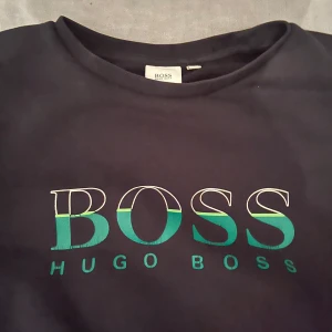 Svart tröja från Hugo Boss - Snygg svart tröja från Hugo Boss med deras ikoniska logga i grönt och blått på bröstet. Tröjan har långa ärmar och en klassisk rund halsringning. Perfekt för en stilren look.