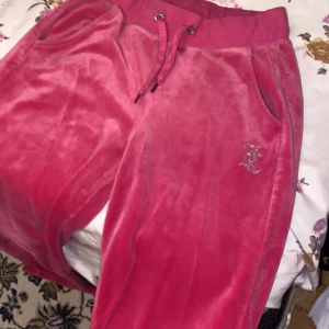 Rosa velourbyxor från Juicy Couture - Snygga rosa velourbyxor från Juicy Couture med glittrande stenar som bildar texten 'Juicy' på baksidan. Byxorna har en bekväm resårmidja med snörning och sidofickor. Perfekta för en avslappnad och trendig look. Skit snygga byxor . Använt några gånger . Storlek xs men är som s  . Vi kan prata om pris tsm . Dom var ändå rätt dyra 