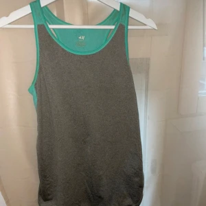 Grå och turkos sportlinne från H&M - Snygg och bekväm grå sportlinne med turkosa detaljer från H&M. Perfekt för varma dagar eller träning. Tillverkad i mjukt material som ger en skön känsla mot huden. Som ny 