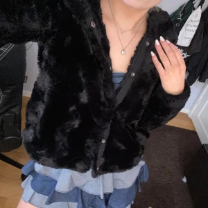 Svart pälsjacka med knappar - Säljer en mysig svart pälsjacka med knappar! Storlek S. Jackan har även luva!