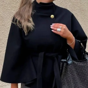 Svart poncho  - Elegant svart kappa med hög krage och knytband i midjan. Den har en unik knappdetalj vid halsen och vida ärmar som ger en stilren look. Perfekt för att höja din outfit till nästa nivå. nyskick med prislapp på.