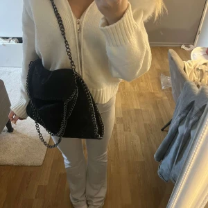 Svart Stella McCartney liknande väska - Snygg svart axelväska med quiltad design och kedjedetaljer. Perfekt för att ge en stilren touch till din outfit. Väskan har en praktisk storlek och är lätt att bära med sig.