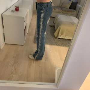 Blå jeans med broderade detaljer - Snygga blå jeans med unika broderade detaljer längs sidorna. De har en klassisk femficksdesign och en bekväm passform. Perfekta för att ge din outfit en cool touch.