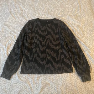Svart glittrig tröja från ONLY - Snygg svart tröja från ONLY med ett glittrigt mönster i silver. Tröjan har långa ärmar och en normal passform, perfekt för att lysa upp vilken outfit som helst. Perfekt att ha på nyår. ✨