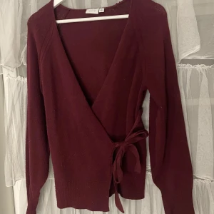 Vinröd omlottkofta från vila - Säljer en vinröd omlottkofta från vila. Koftan har långa ärmar och knytband i midjan för en justerbar passform. Perfekt för höst och vinter med sitt mysiga material.