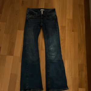 Blå jeans från Gina Tricot - Snygga blå jeans från Gina Tricot med bootcut-stil. De har en klassisk femficksdesign och stängs med dragkedja och knappar. Perfekta för en avslappnad look.
