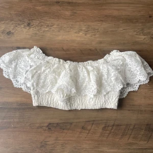Vit spetsig offshoulder topp från Fashion Nova - Säljer en söt vit offshoulder topp från Fashion Nova. Toppen är dekorerad med vacker spets och har en elastisk kant för en bekväm passform🌸