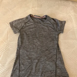 Grå kortärmad träningströja - Säljer en grå kortärmad träningströja i syntetmaterial. Perfekt för gymmet eller löprundan. Tröjan har en melerad design och rund halsringning.