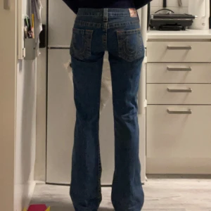 True Religion jeans - Snygga blå jeans från True Religion med klassisk femficksdesign och tydliga sömmar. De har en låg midja . Perfekta för en casual outfit. Tyvärr lite förstora på mig som brukar bära 34 eller xs, som referens är jag 171cm 💗 tråden har lossnat lite på lappen men det är nog något som går att fixa själv 😊 