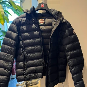 Svart dunjacka från Colmar - Säljer en snygg svart dunjacka från Colmar. Jackan har en pufferdesign med dragkedja och huva, perfekt för kyliga dagar. Den är långärmad och har en stilren look med Colmar-logga på ärmen. Passar perfekt för vintern och hösten. Det är bara att skriva om ni har ytterligare funderingar om jackan!Kan gå ner i pris vid snabb affär 