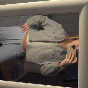 Grå croppad jacka - Snygg grå croppad jacka med dragkedja och knappar framtill. Jackan har en stilren design med långa ärmar och två stora fickor på bröstet. Perfekt för en trendig look!